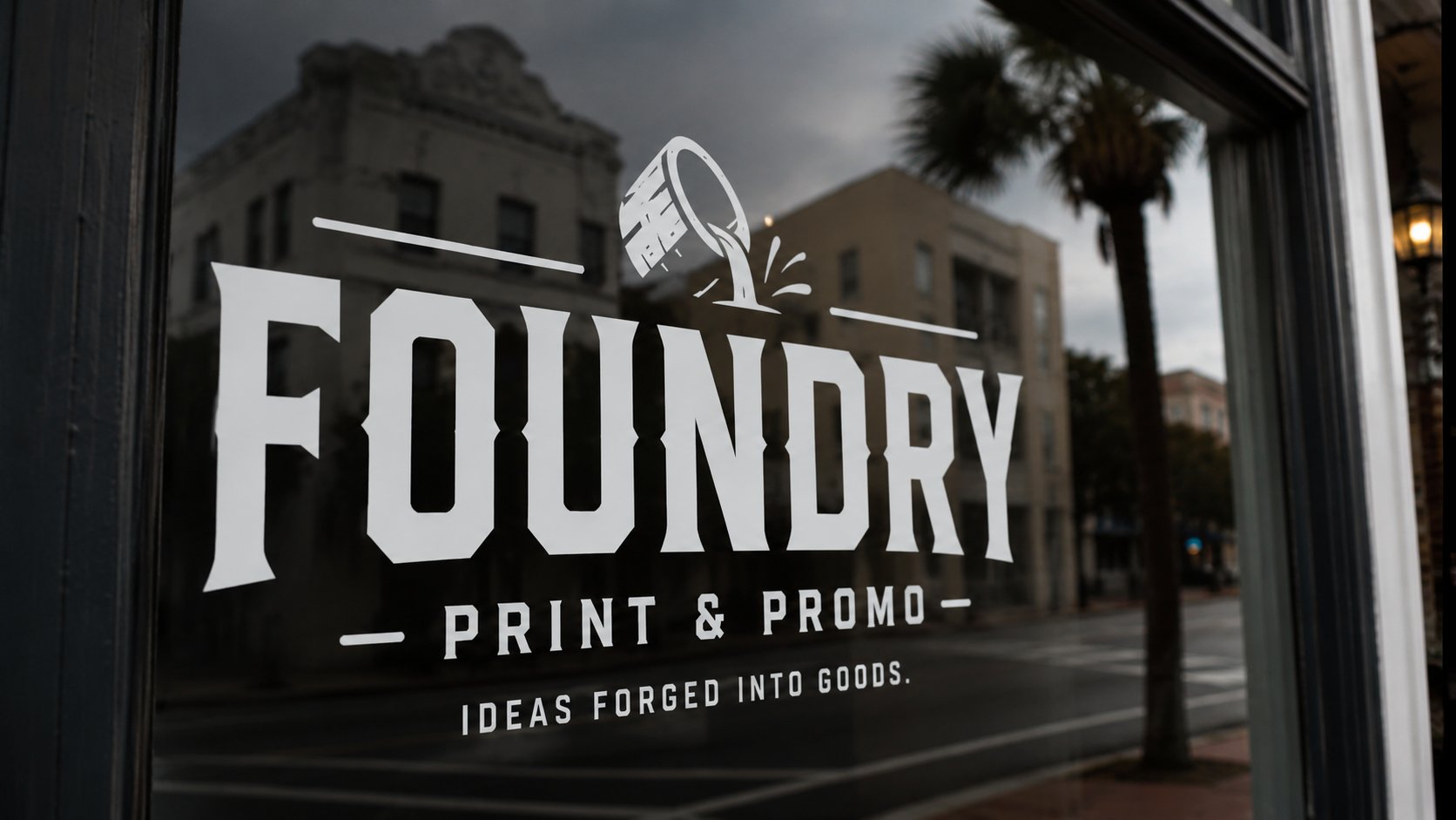 Foundry Print and Promo logo applied as a window decal on a Charleston, SC storefront — downtown architecture and palm tree reflected in glass